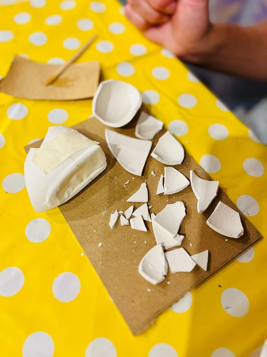 Frammenti di un cuore in ceramica su un cartone, tavolo giallo a pois